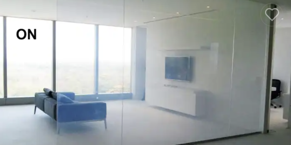 Un salon moderne dispose de murs en verre avec Film dépoli à cristaux liquides, d'un canapé bleu, d'une télévision murale et de grandes fenêtres offrant une vue à couper le souffle.